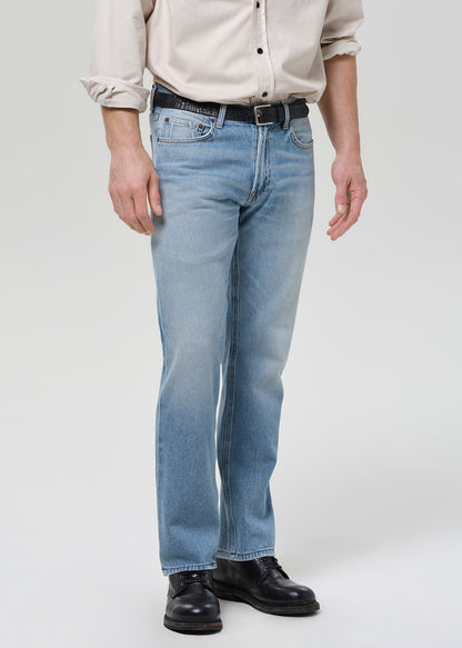 Person wearing a beige shirt and light blue jeans on a grey background.