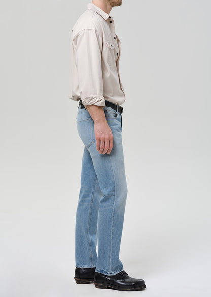 Person wearing a beige shirt and light blue jeans on a grey background.