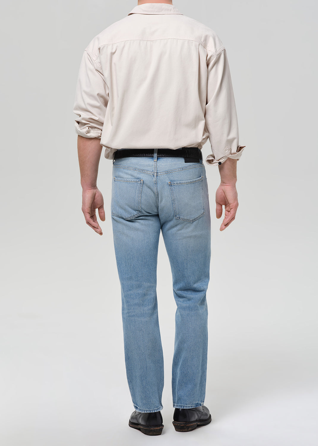 Person wearing a beige shirt and light blue jeans on a grey background.