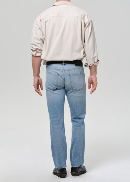 Person wearing a beige shirt and light blue jeans on a grey background.