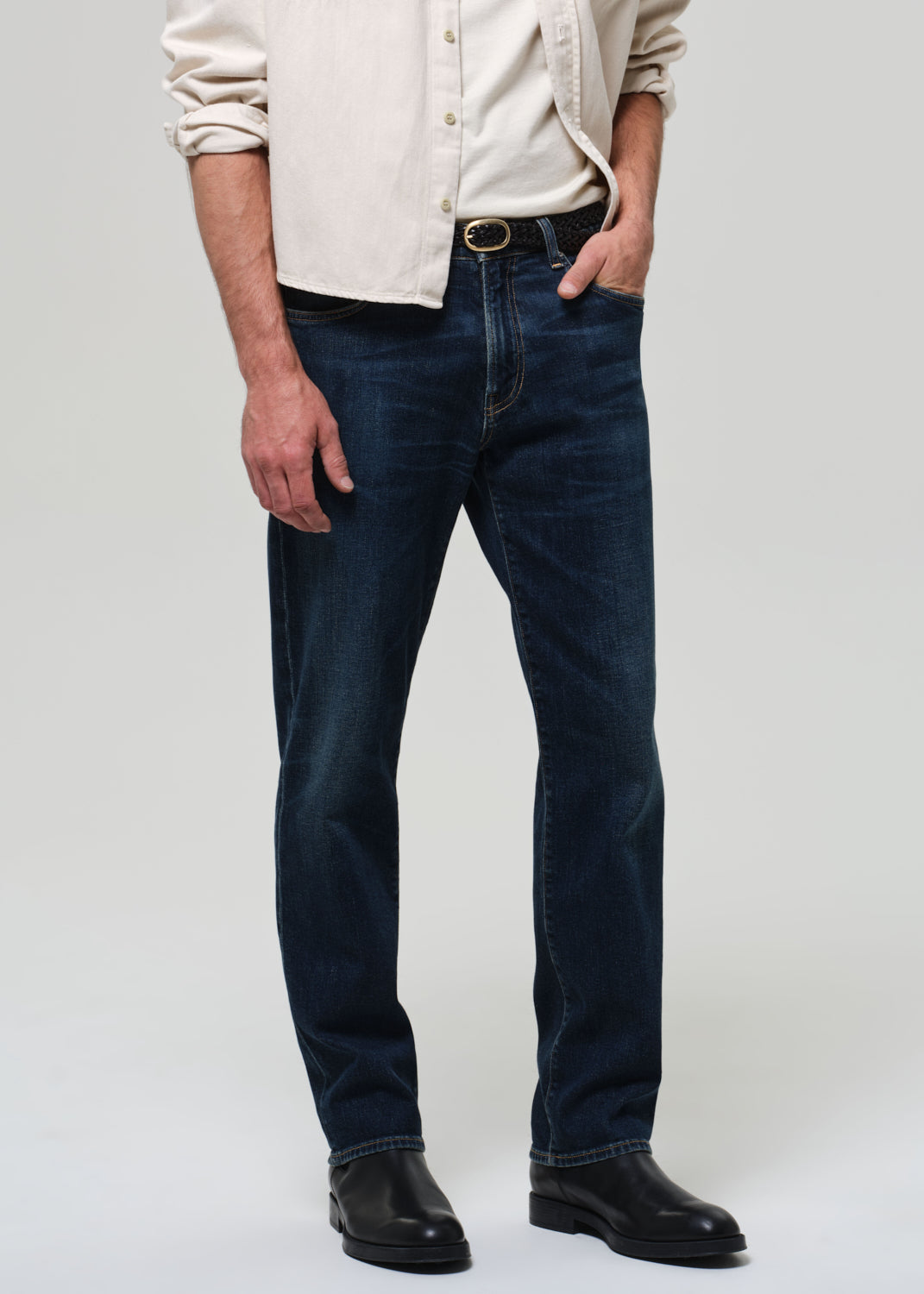 Person wearing dark blue jeans and a light-colored shirt on a plain background