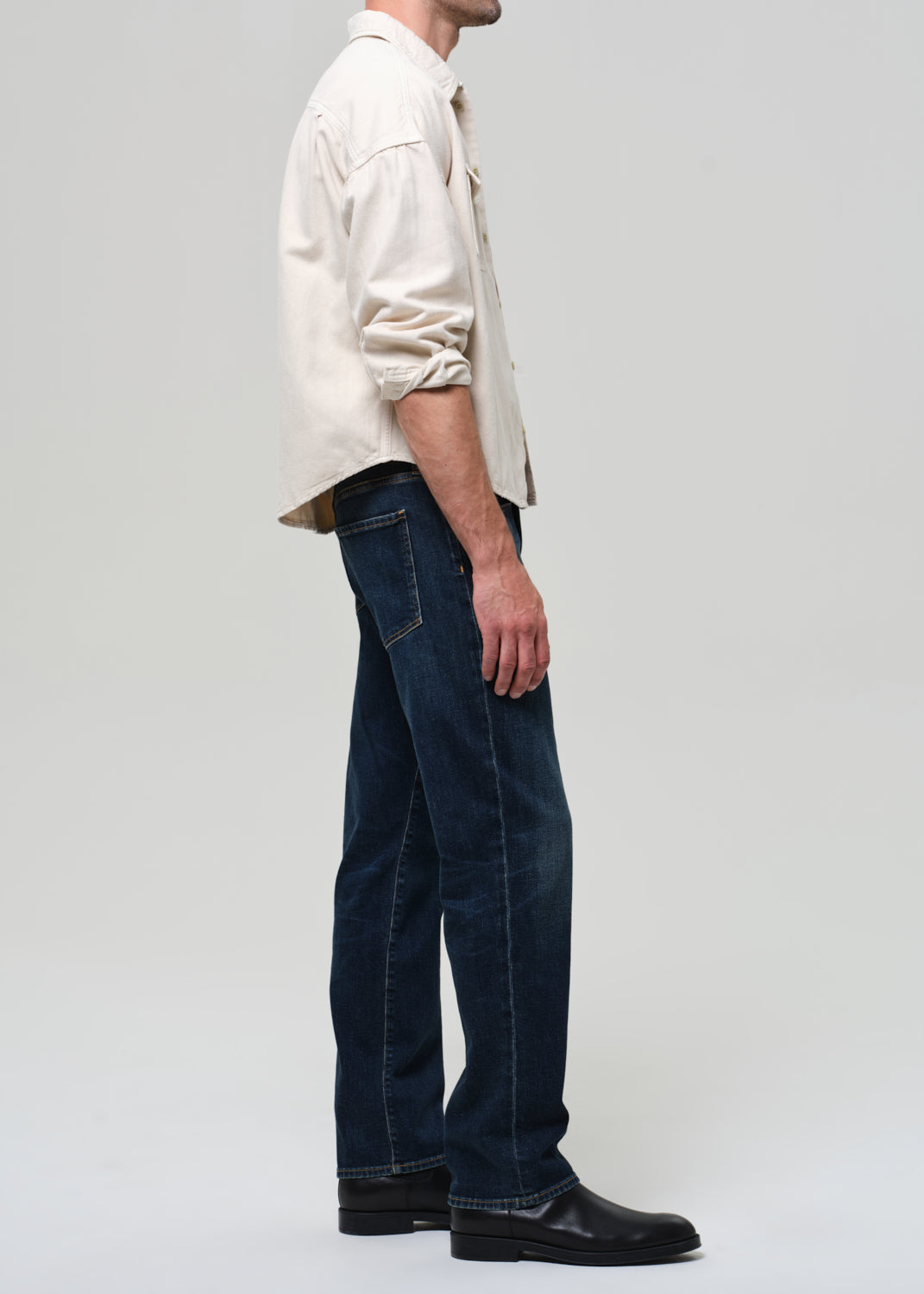 Person wearing a light-colored shirt and dark jeans on a plain background