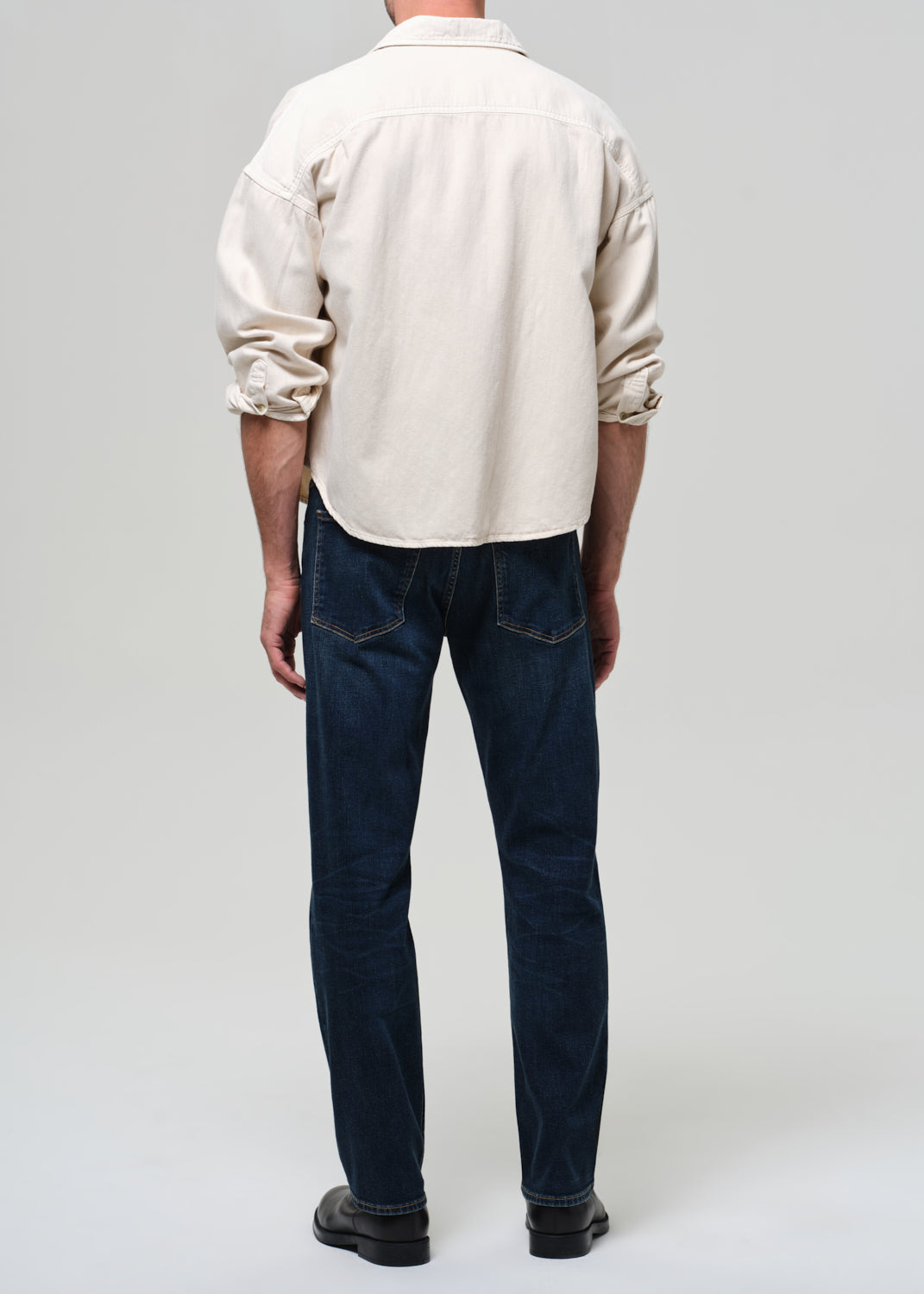 Person wearing a beige shirt and dark blue jeans on a plain background