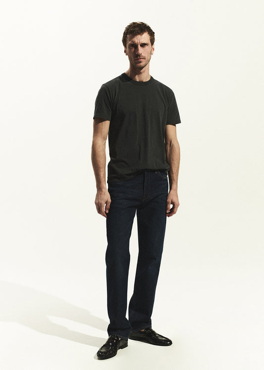 Man wearing a grey t-shirt and dark wash jeans on a white background