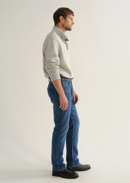 Person wearing medium blue straight leg jeans with a light grey long sleeve collared pullover and black boots, side full body view on a light grey background.