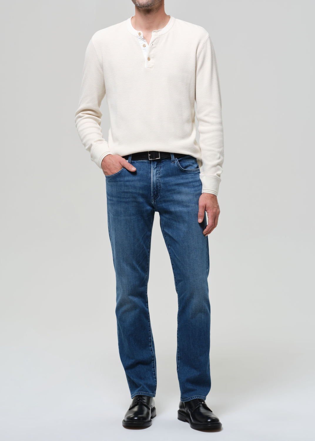 Person wearing a white sweater and blue jeans on a plain background