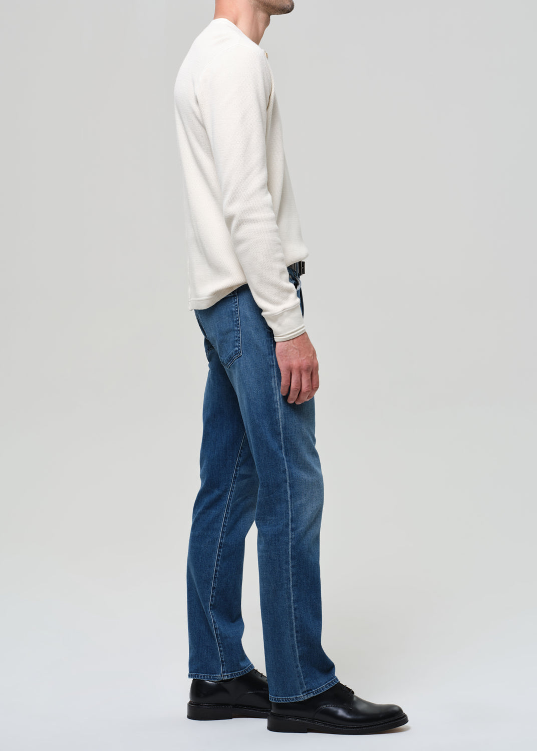 Person wearing a white sweater and blue jeans on a plain background