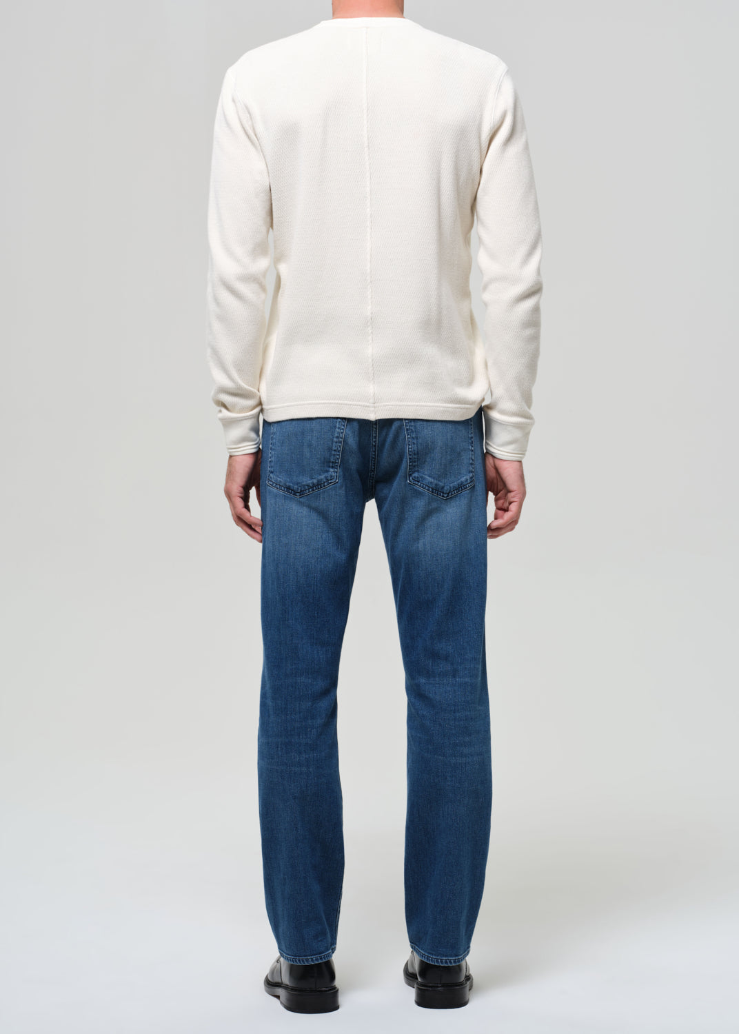 Person wearing a white sweater and blue jeans on a plain background