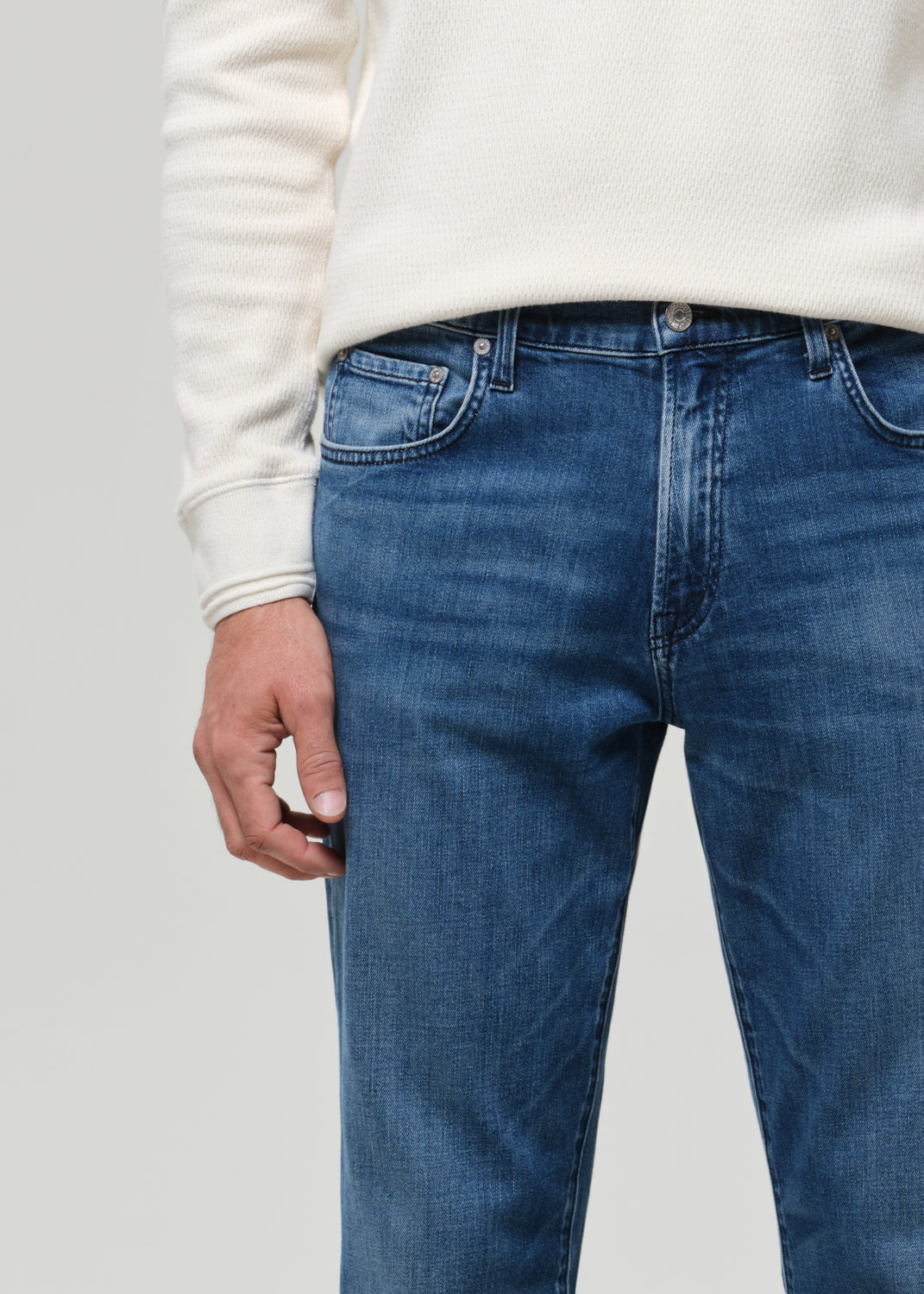 Person wearing blue jeans and a white sweater on a light gray background