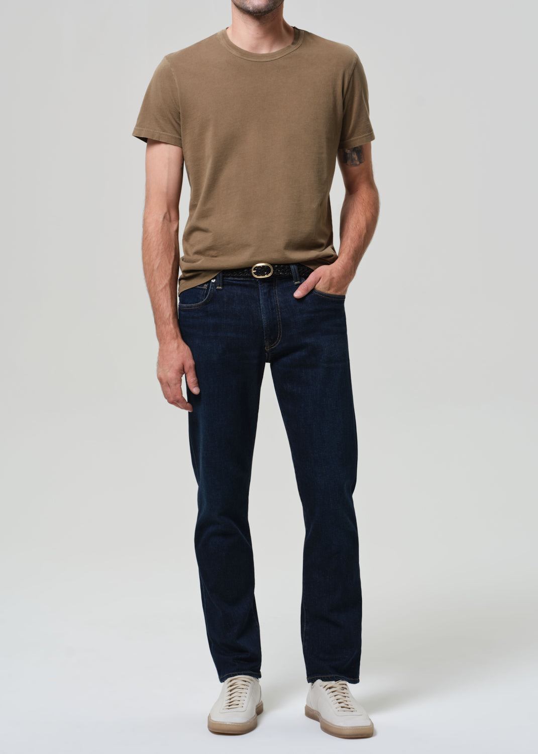 Man wearing a brown t-shirt and dark jeans on a plain background