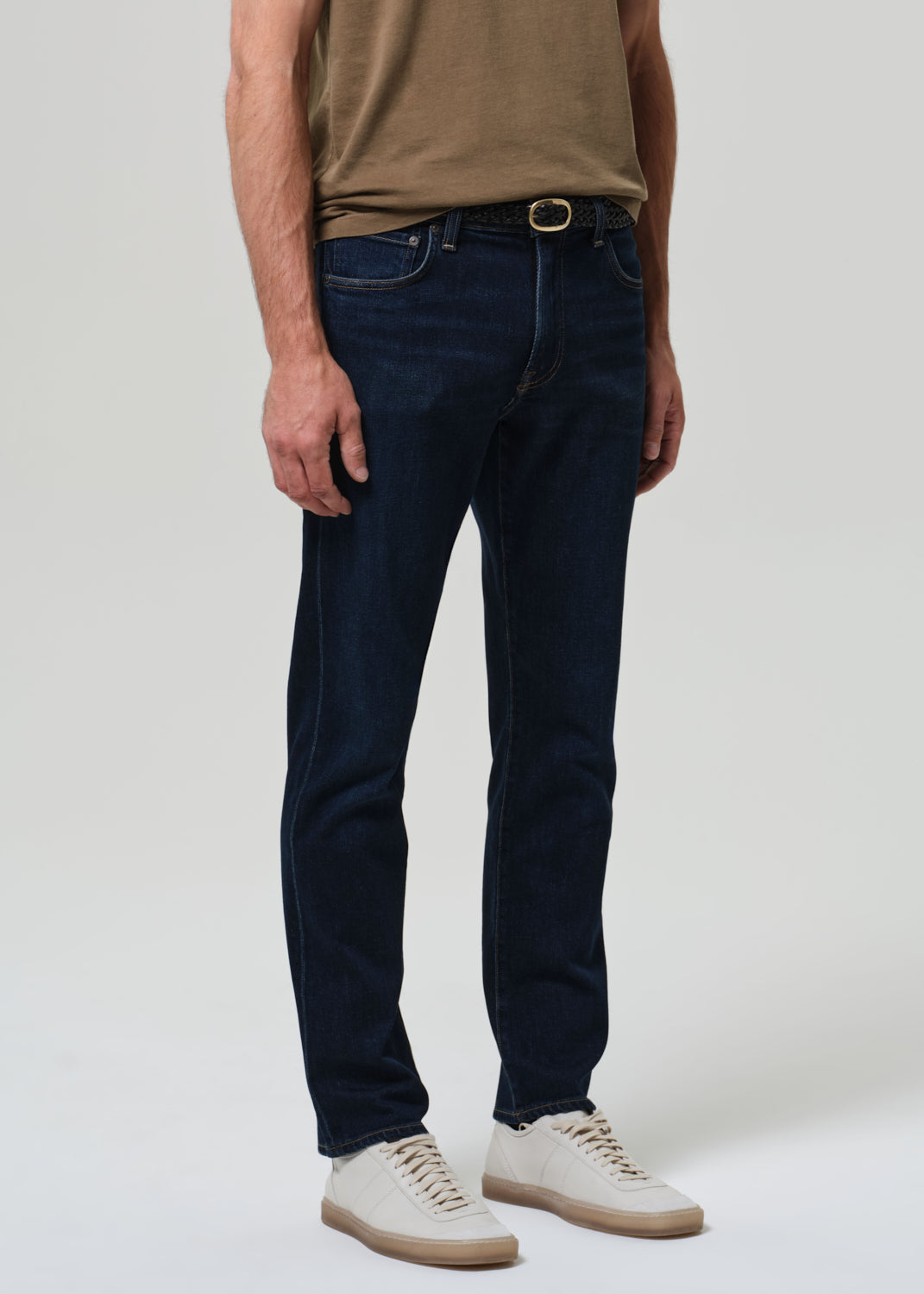 Person wearing dark blue jeans and a brown shirt on a white background