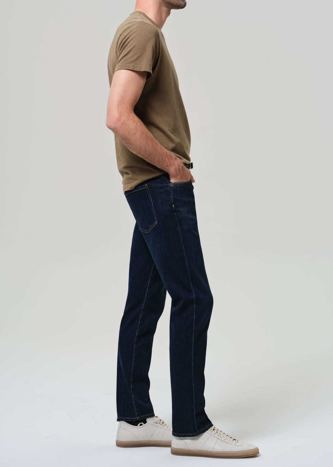 Man wearing a brown t-shirt and dark blue jeans on a white background