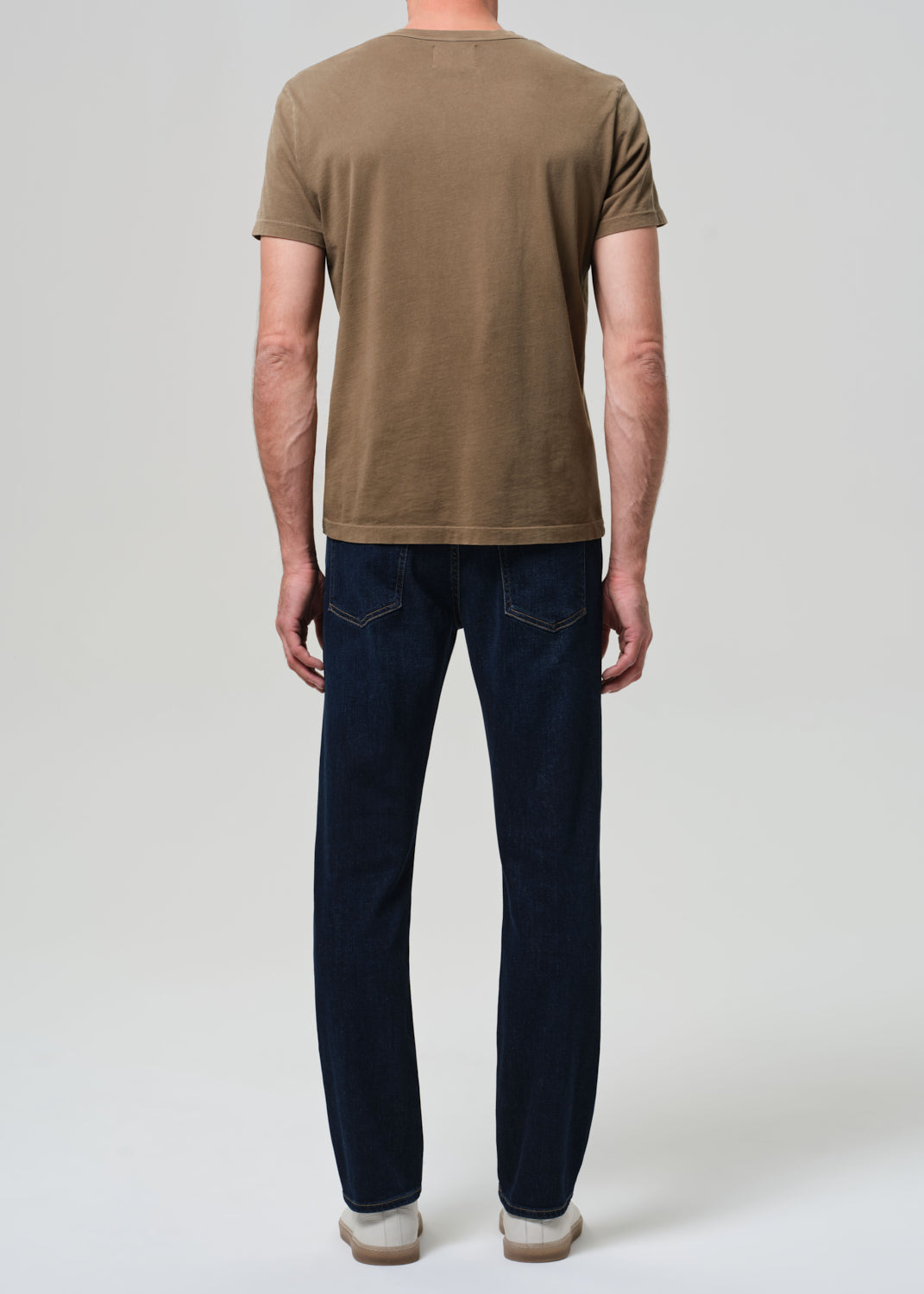 Person wearing a brown t-shirt and dark blue jeans on a plain background