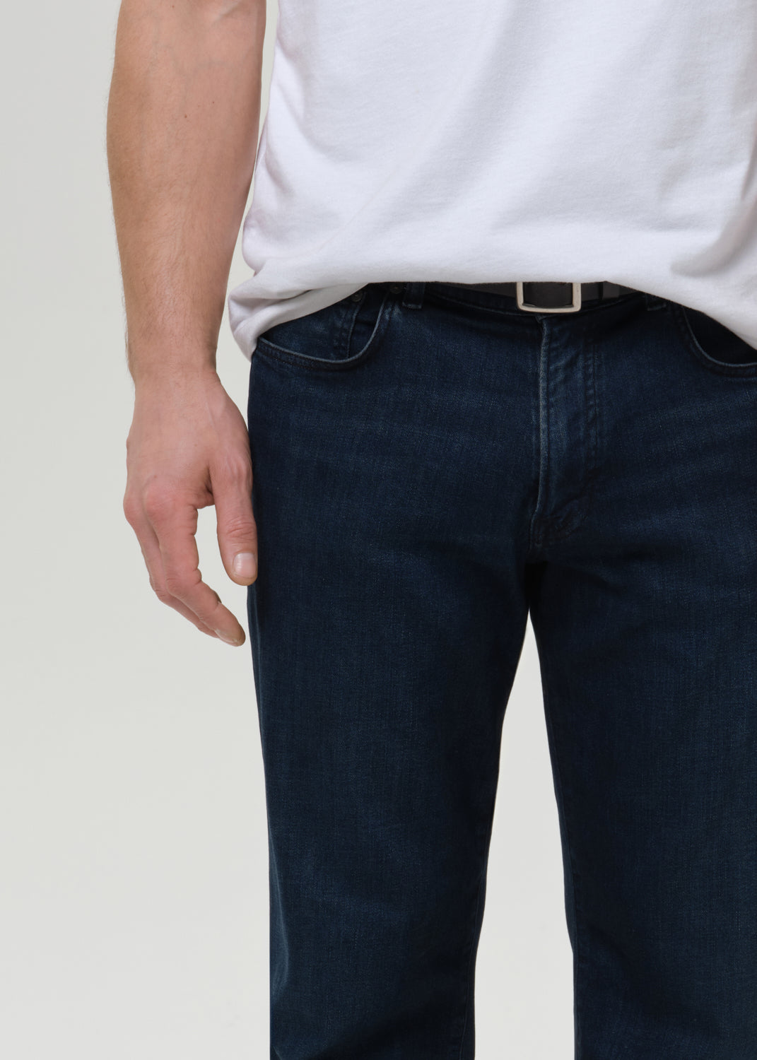 Person wearing dark blue jeans and a white shirt on a plain background