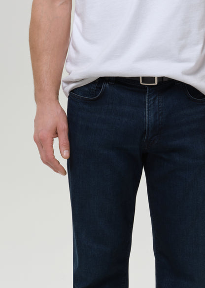 Person wearing dark blue jeans and a white shirt on a plain background