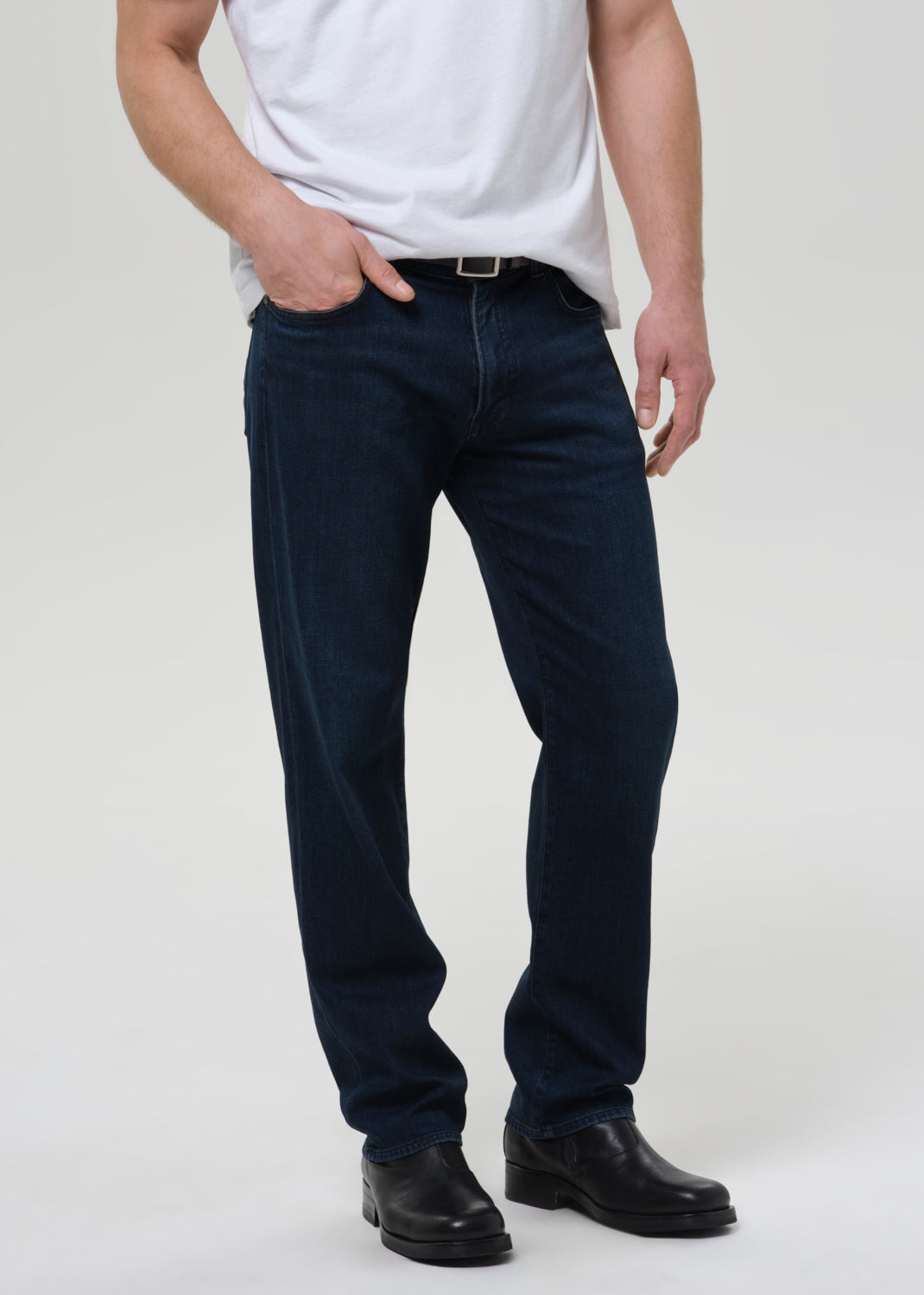 Person wearing navy blue jeans and a white shirt on a plain background