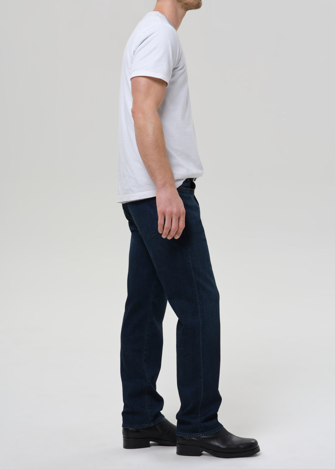 Person wearing a white t-shirt and dark jeans on a plain background