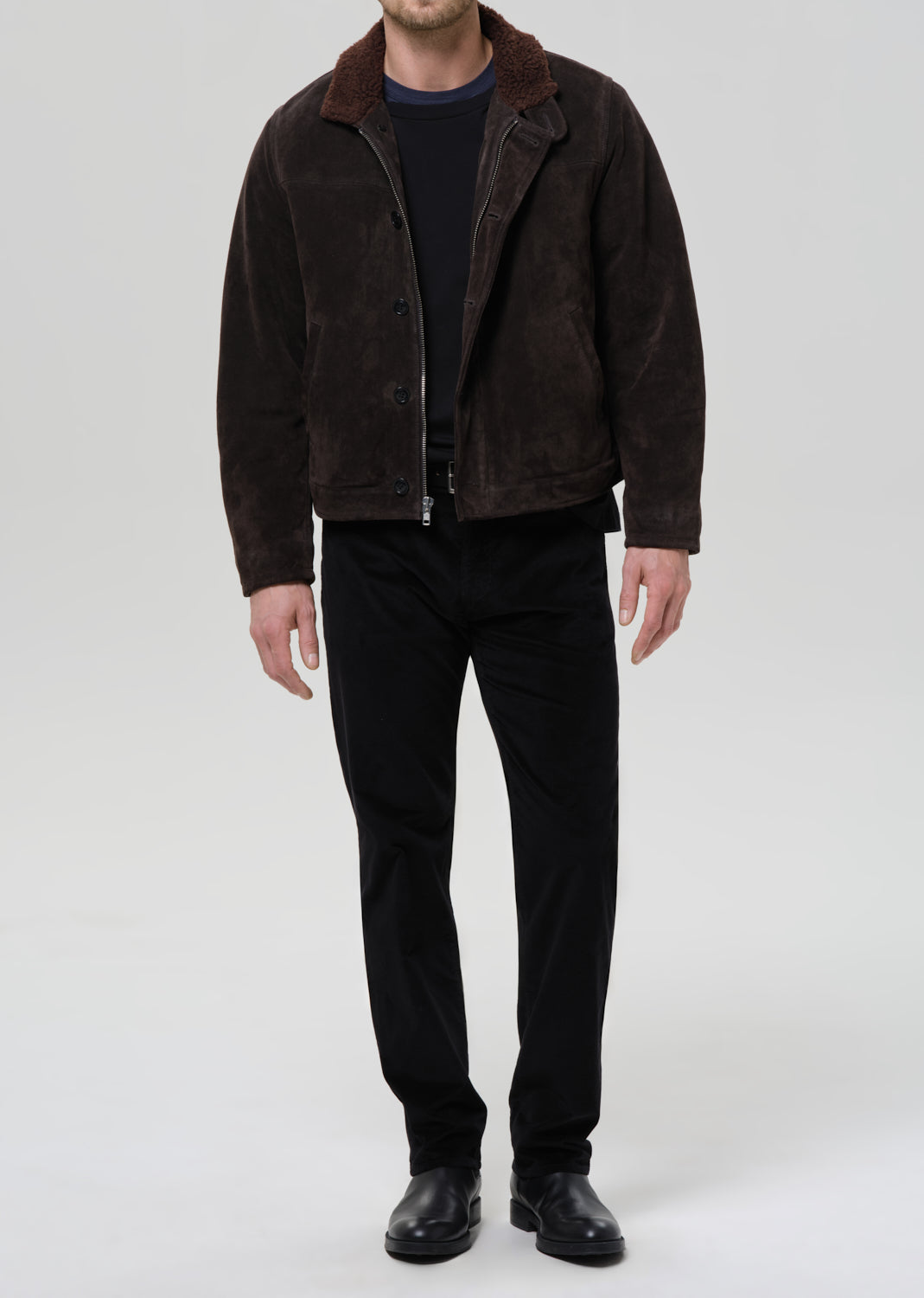 Man wearing a brown suede jacket and black pants on a grey background