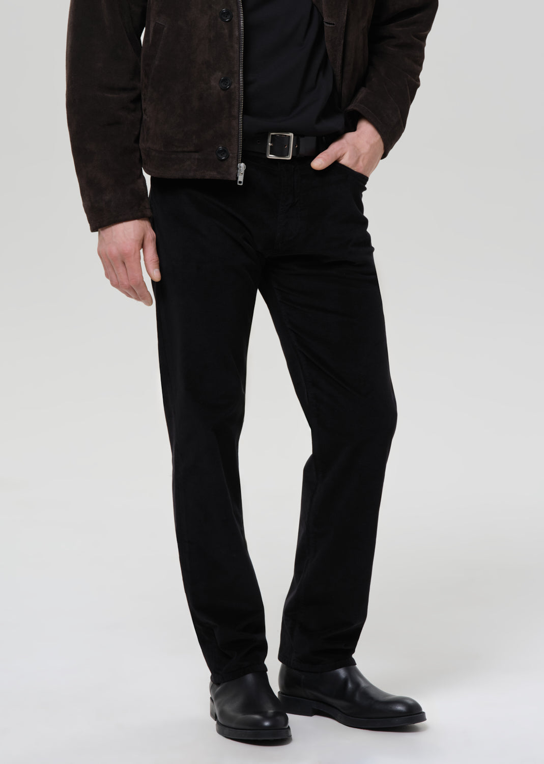 Person wearing a dark jacket, black shirt, and black pants on a grey background