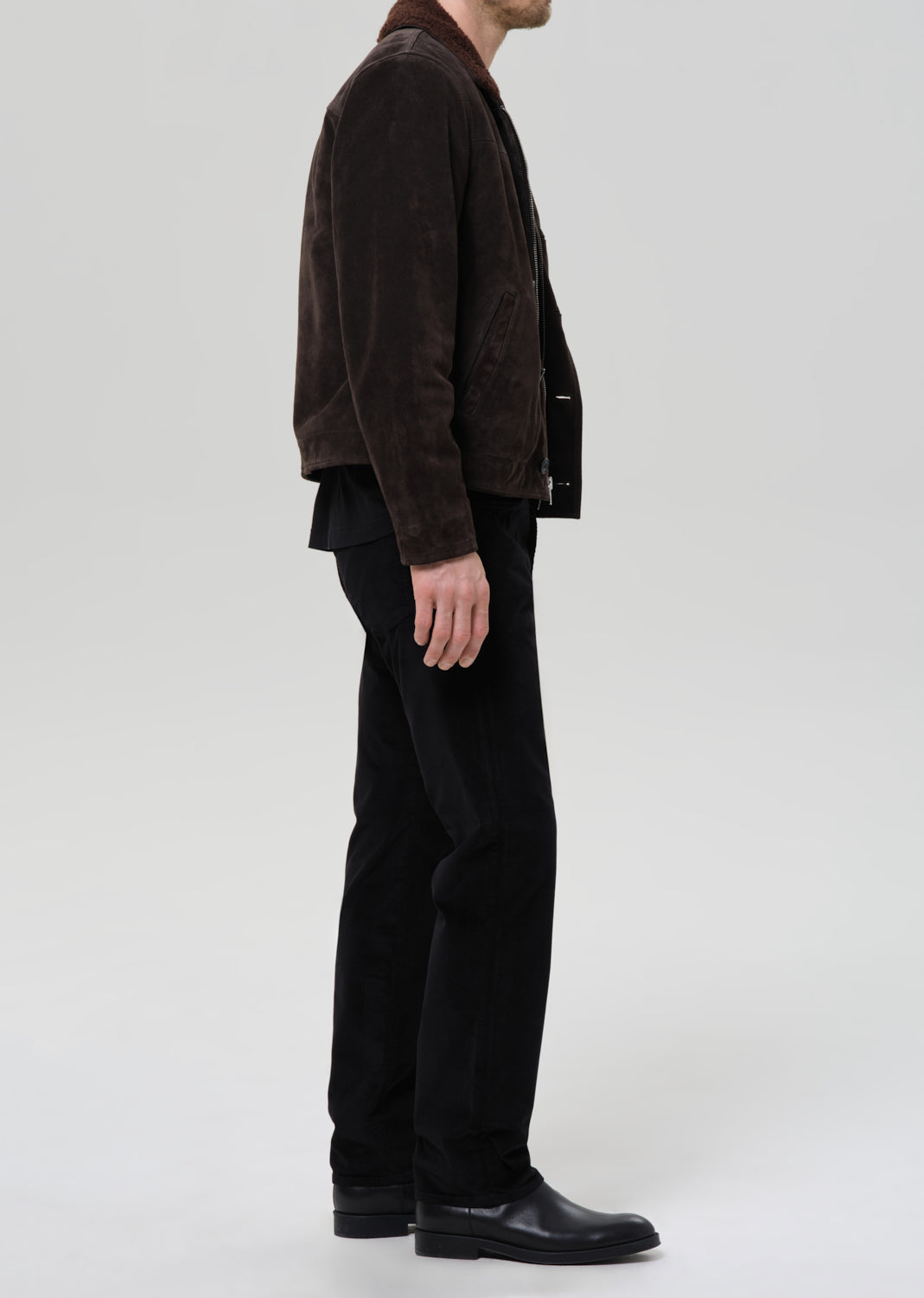 Person wearing a brown jacket and black pants on a grey background