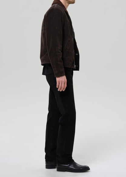 Person wearing a brown jacket and black pants on a grey background