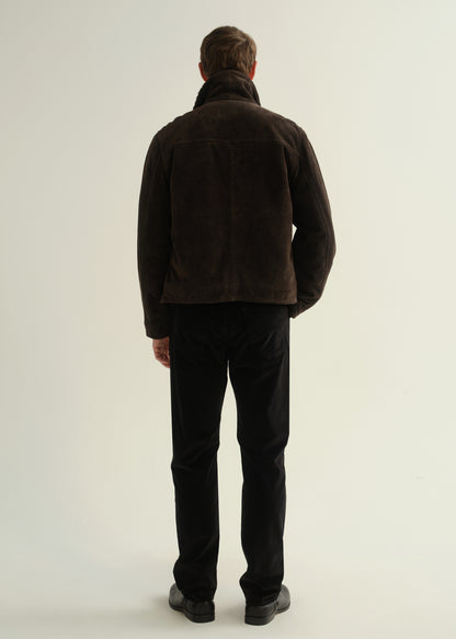 Person wearing black straight leg jeans with a dark brown jacket and black boots, back full body view on a light grey background.