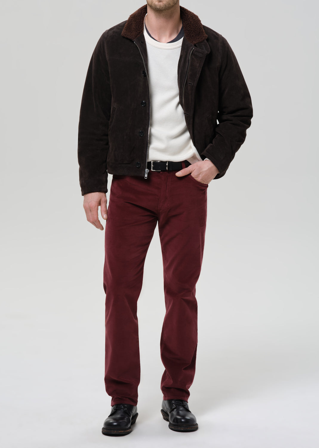 Man wearing a dark jacket, white shirt, and red pants on a grey background