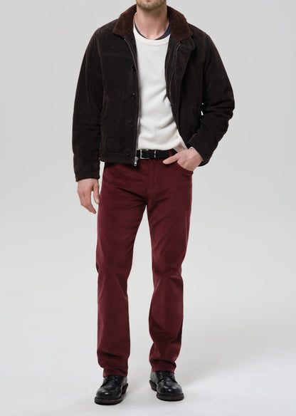 Man wearing a dark jacket, white shirt, and red pants on a grey background