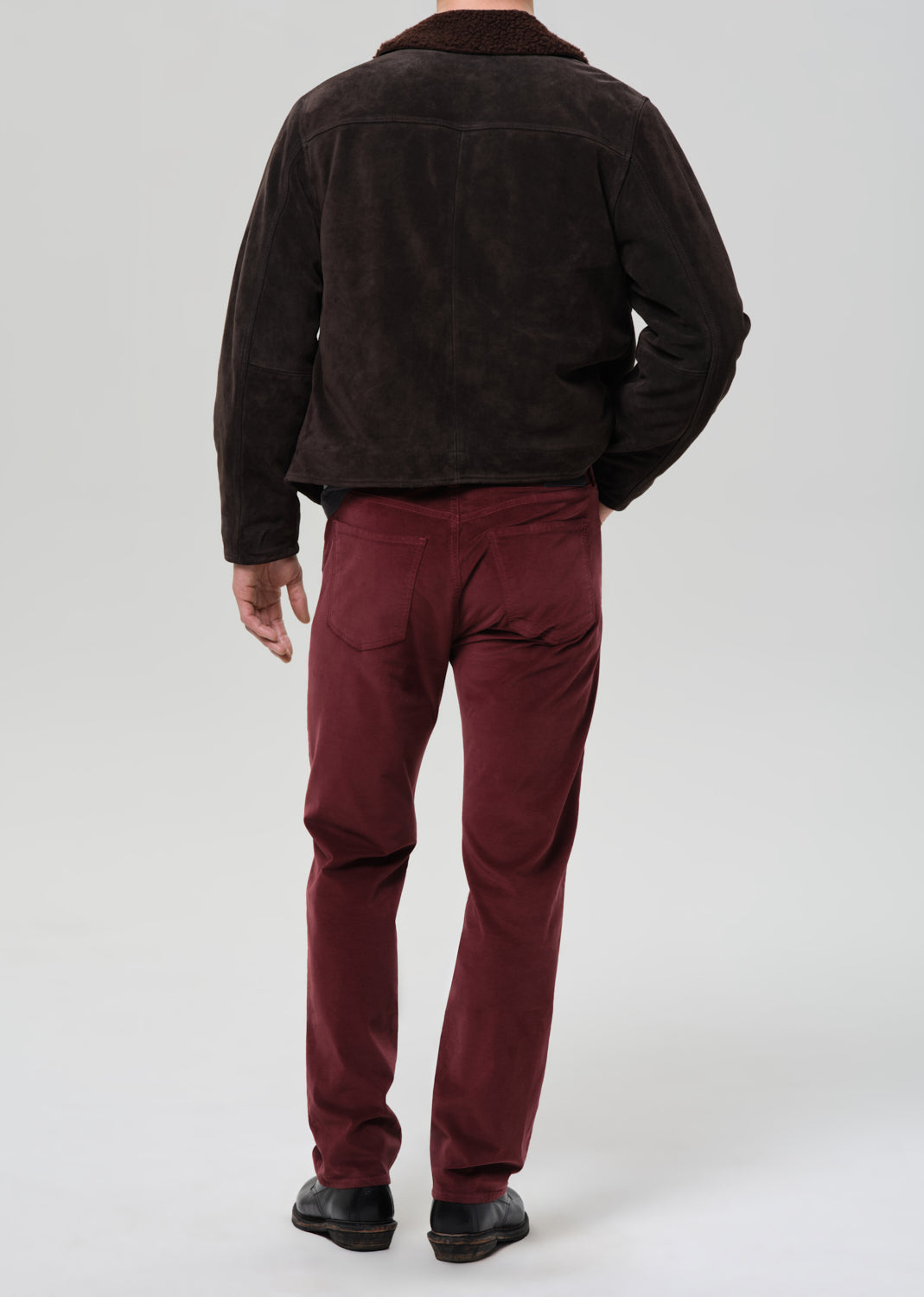 Person wearing a dark brown jacket and red pants on a grey background