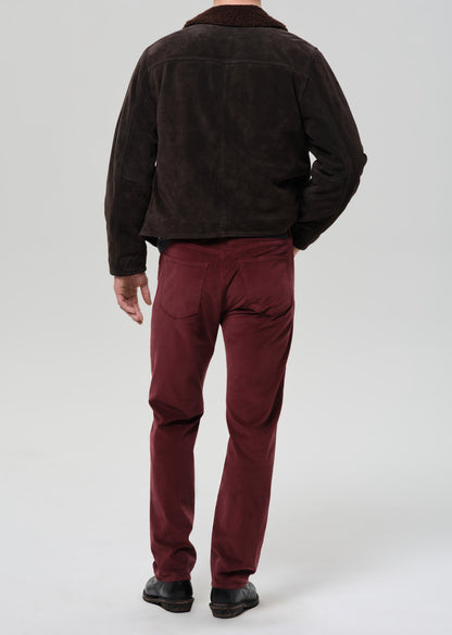 Person wearing a dark brown jacket and red pants on a grey background