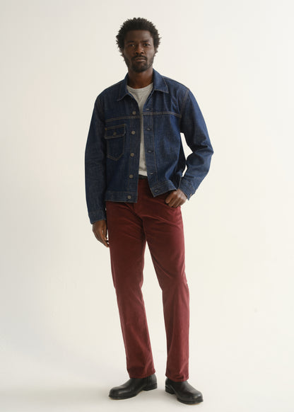 Person wearing burgundy straight leg pants with a medium blue denim jacket, dark shirt, and black shoes, front full body view on a light grey background.