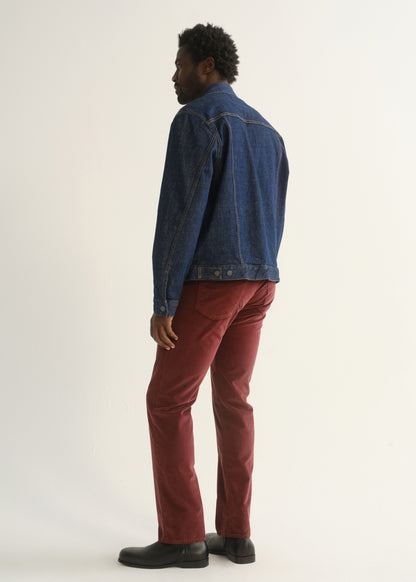 Person wearing burgundy straight leg pants with a medium blue denim jacket and black shoes, back full body view on a light grey background.