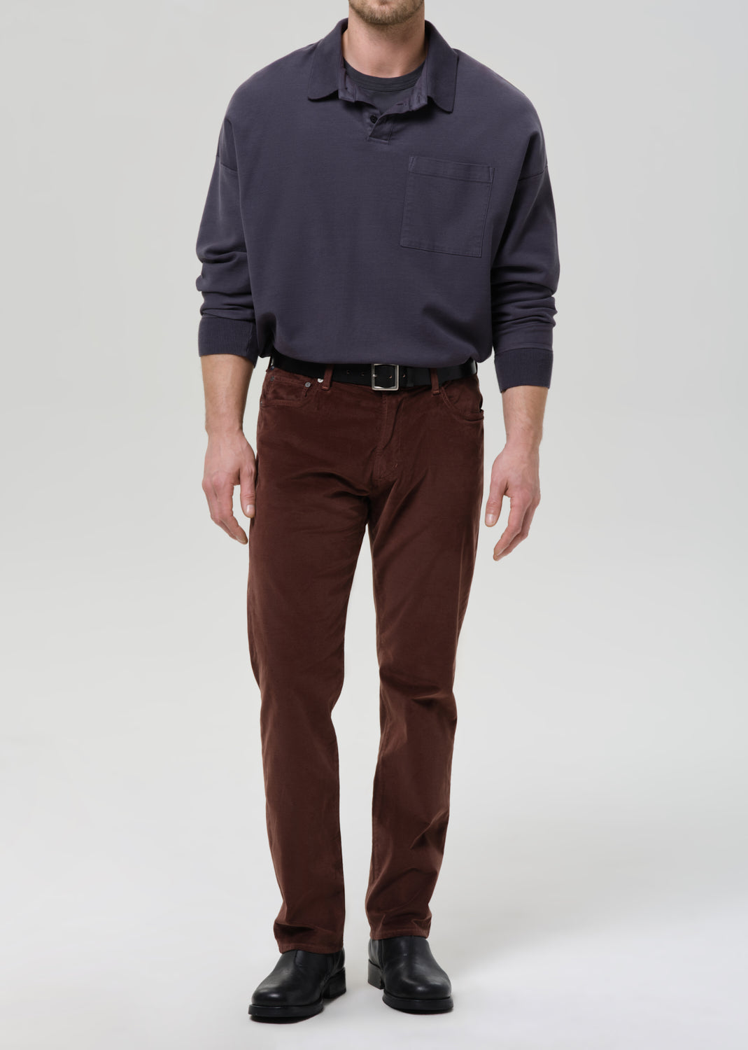 Man wearing a dark sweater and brown pants on a grey background