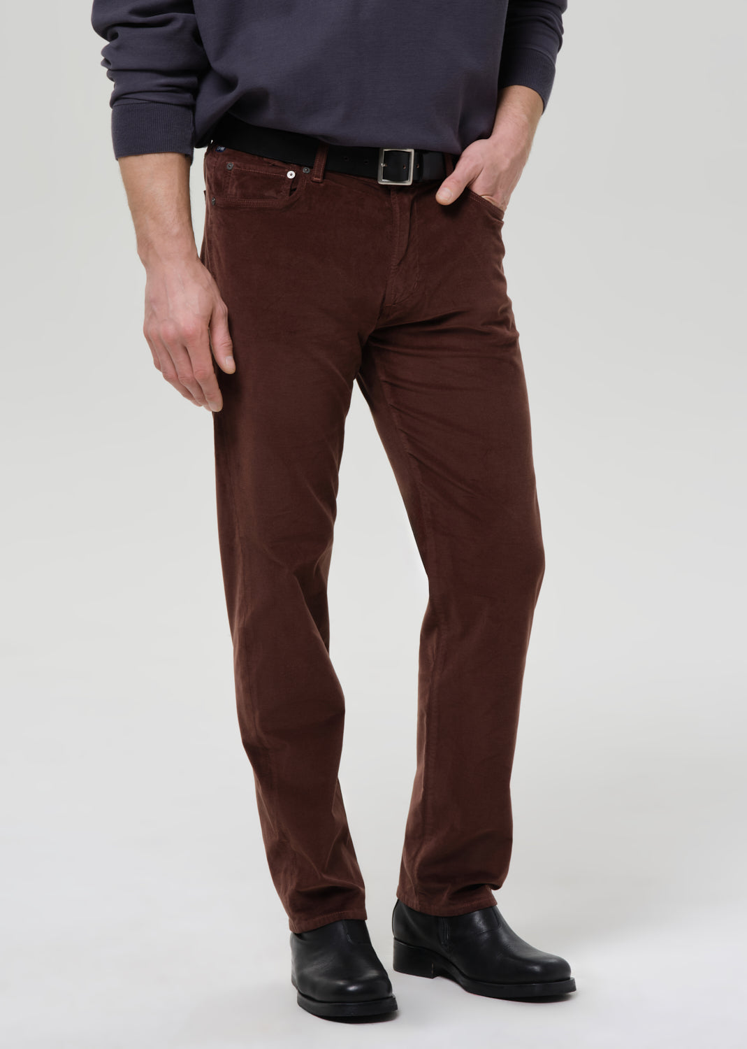 Person wearing brown pants and black shoes on a grey background