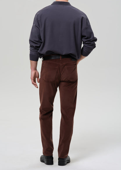 Person wearing a dark sweater and brown pants on a grey background