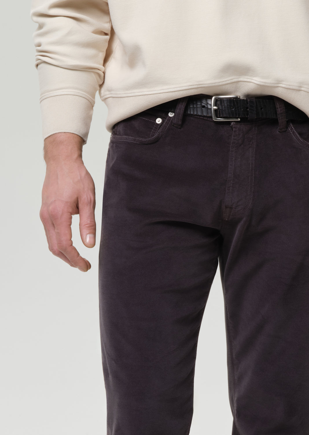 Person wearing dark pants and a beige sweater on a grey background
