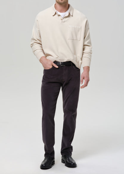Man wearing a beige sweater and dark pants on a grey background