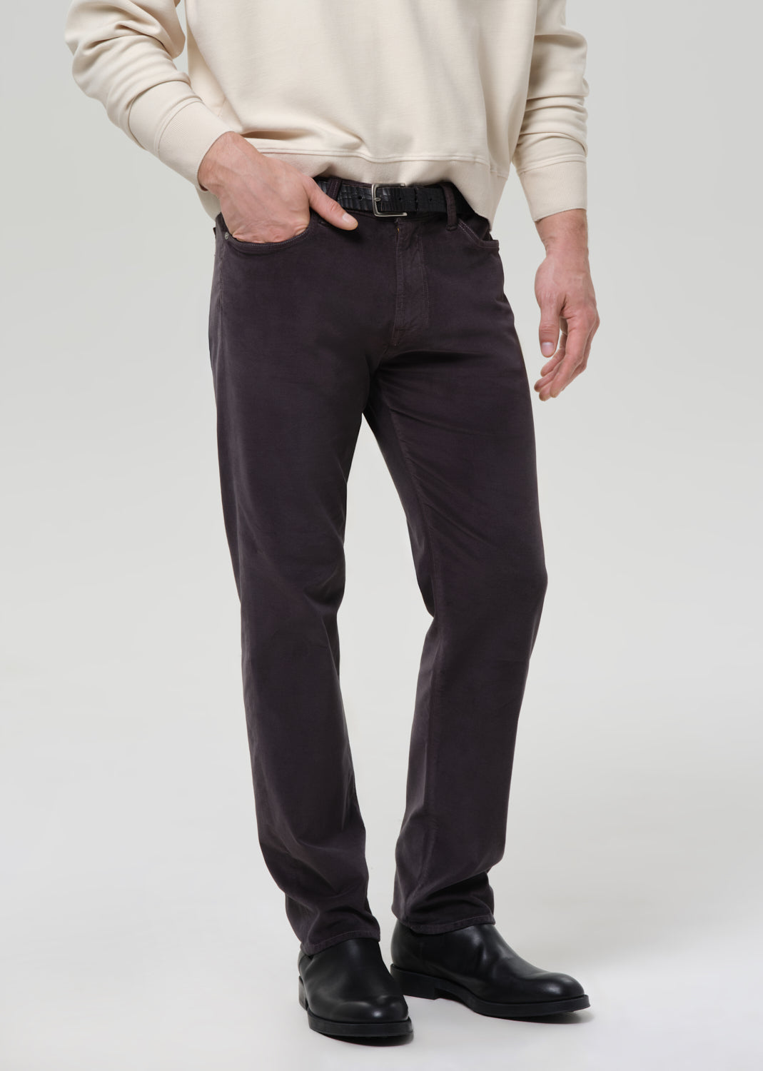 Person wearing dark pants and a beige sweater on a grey background
