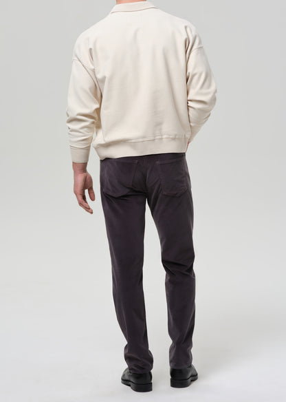Person wearing a beige sweater and dark pants on a grey background