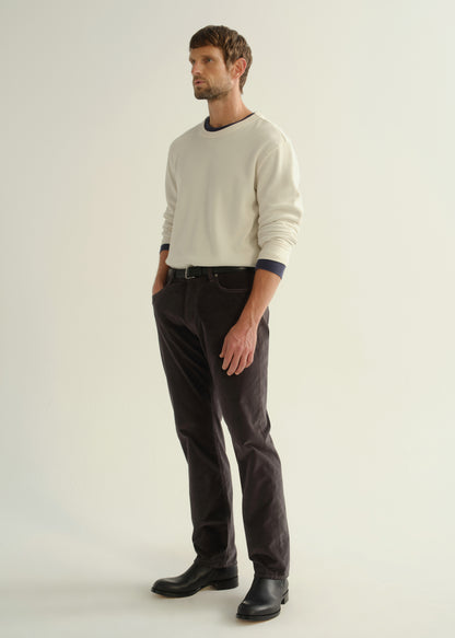 Person wearing dark charcoal straight leg jeans with a cream long sleeve shirt and black boots, angled front full body view on a light grey background.