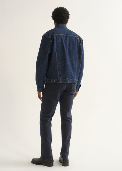 Person wearing dark indigo straight leg jeans with a medium blue denim jacket and black shoes, back full body view on a light grey background.