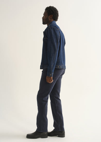 Person wearing dark indigo straight leg jeans with a medium blue denim jacket and black shoes, angled front full body view on a light grey background.