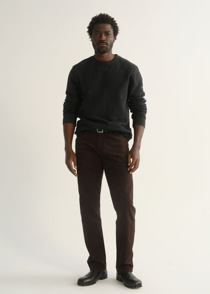 Person wearing dark brown straight leg pants with a dark charcoal long sleeve crewneck sweater and black shoes, front full body view on a light grey background.