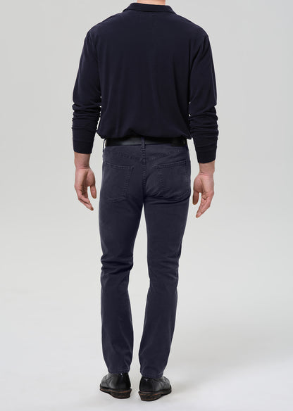 A man viewed from the back wearing a dark navy long-sleeve shirt, dark navy pants, and black shoes, standing against a grey background.