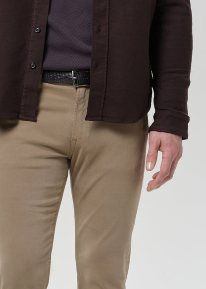 A close-up of a person wearing tan chinos, a dark brown button-up shirt, and a dark purple knit top, with a black belt, against a grey background.