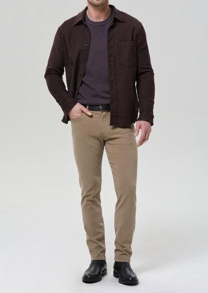 A man modeling a dark brown button-up shirt over a dark grey t-shirt, paired with khaki pants and black boots, against a grey background.