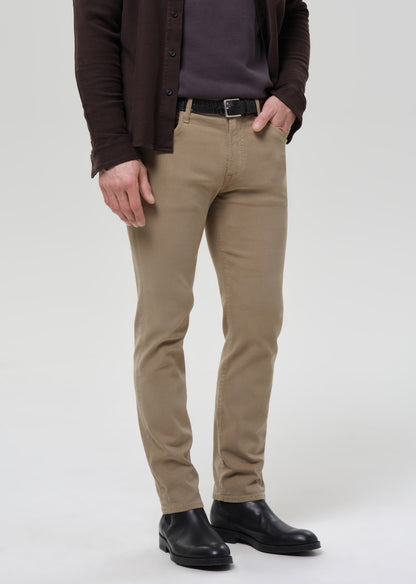 A person wearing slim-fit tan chinos with a dark brown button-up shirt, dark brown cardigan, black belt, and black leather boots, shown from the chest down on a grey background.