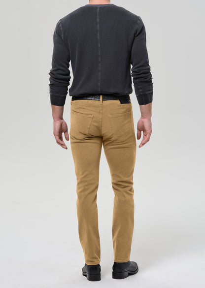 A man viewed from the back wearing slim-fit tan chinos, a dark charcoal grey long-sleeve shirt, and black shoes, against a grey background.
