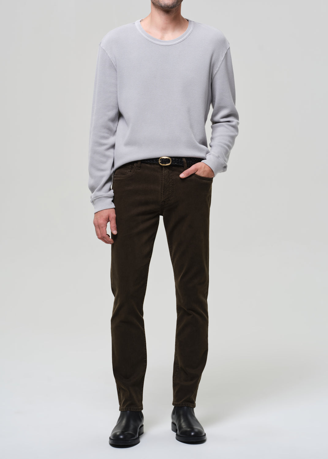 Person wearing a light gray sweater and brown pants on a white background