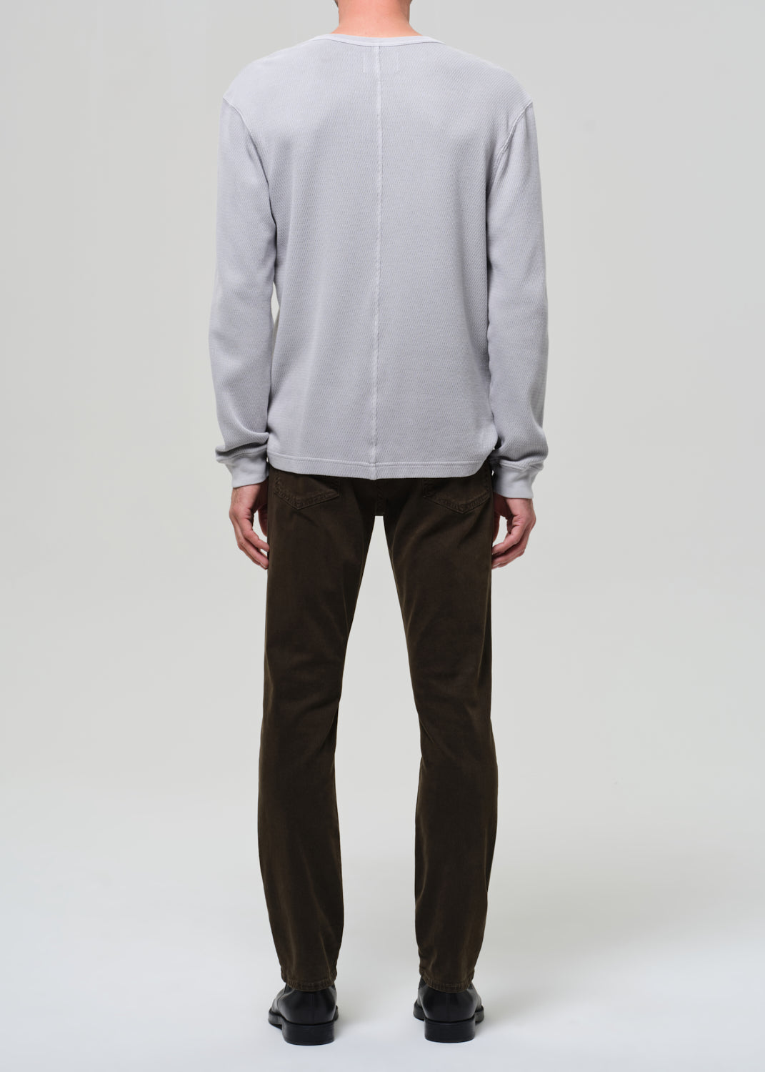 Person wearing a light gray sweater and dark brown pants on a white background